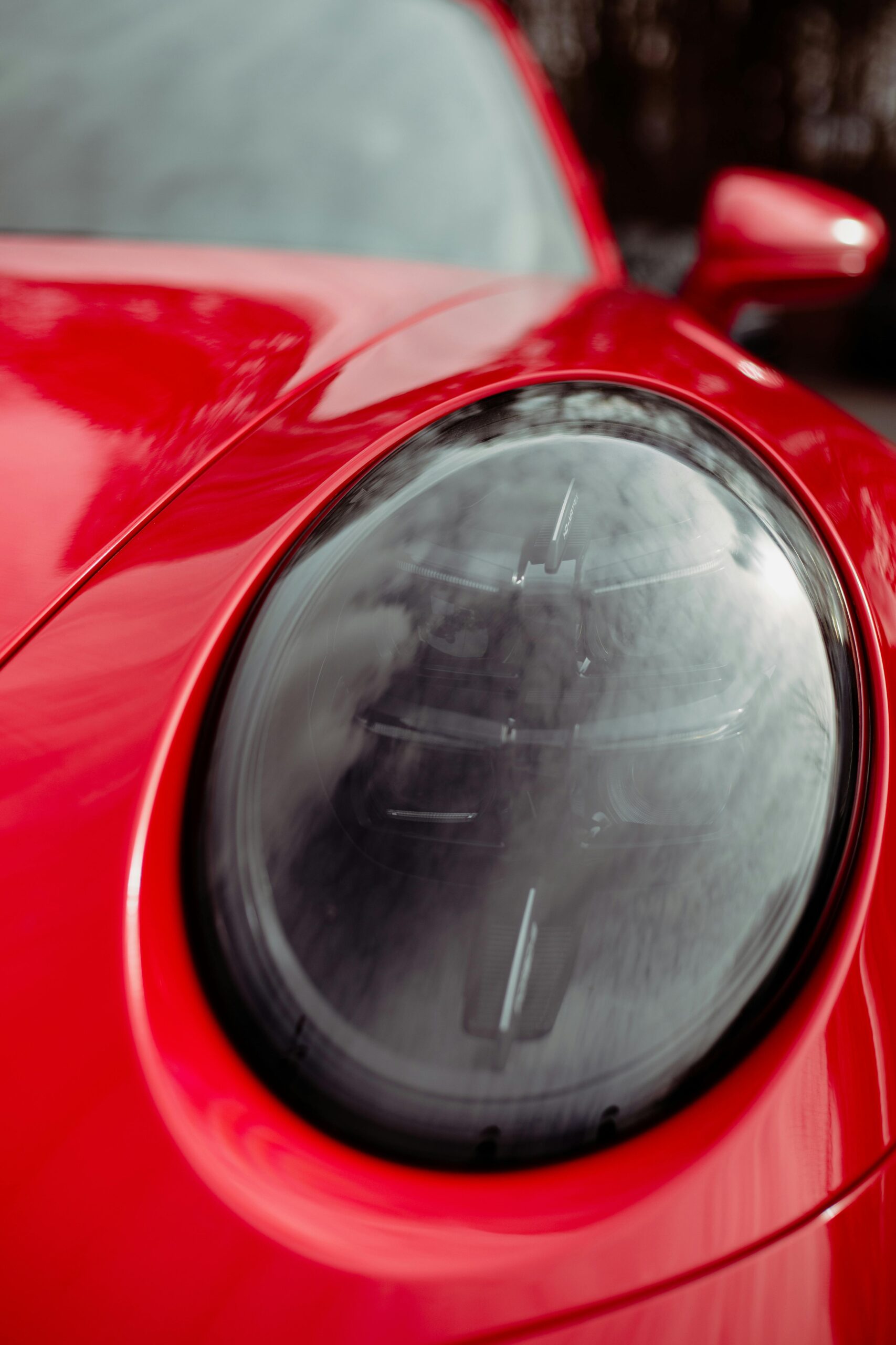 Detailed close-up of a red sports car headlight showcasing sleek design and glossy finish.