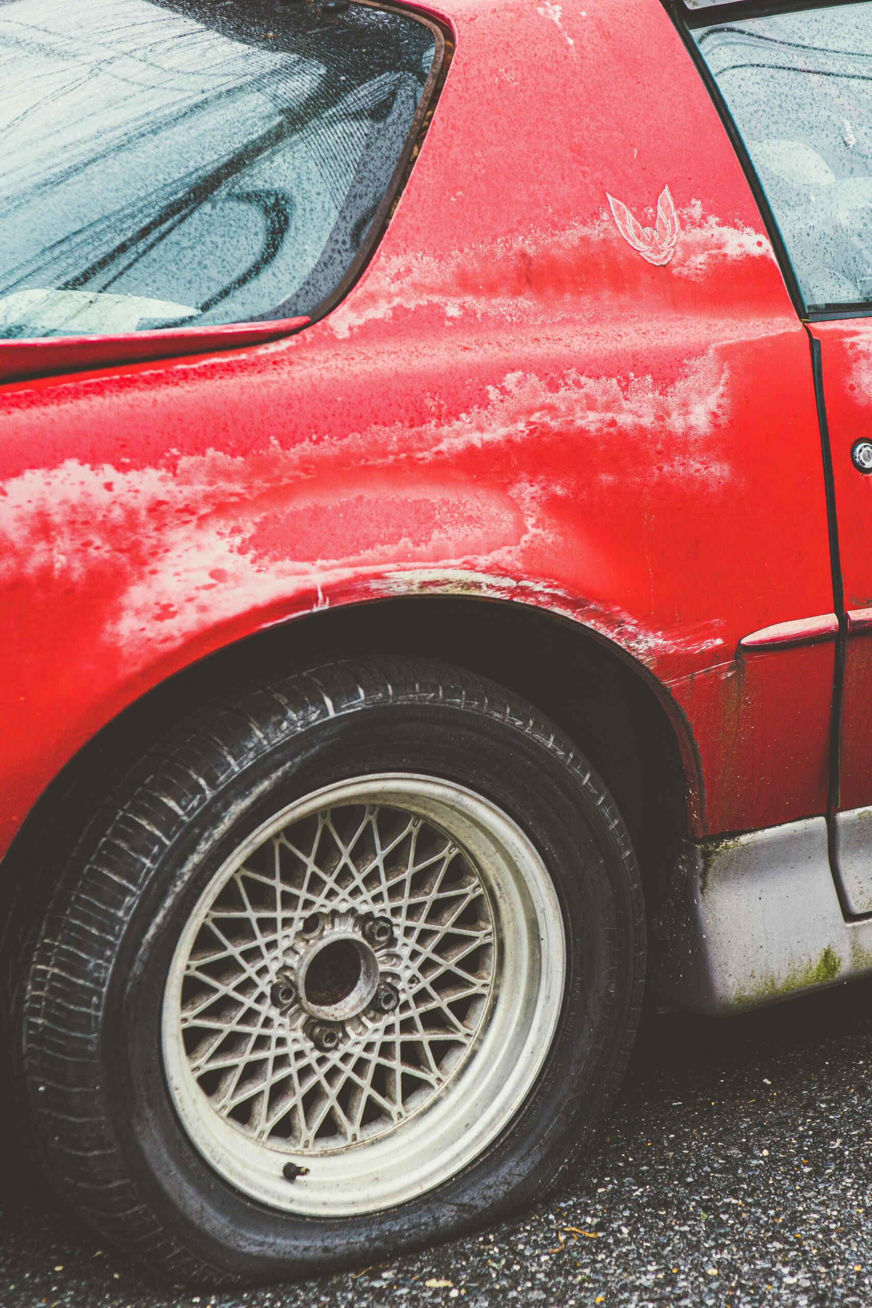 A weathered red car with a flat tire, showcasing aged automobile details and rust.